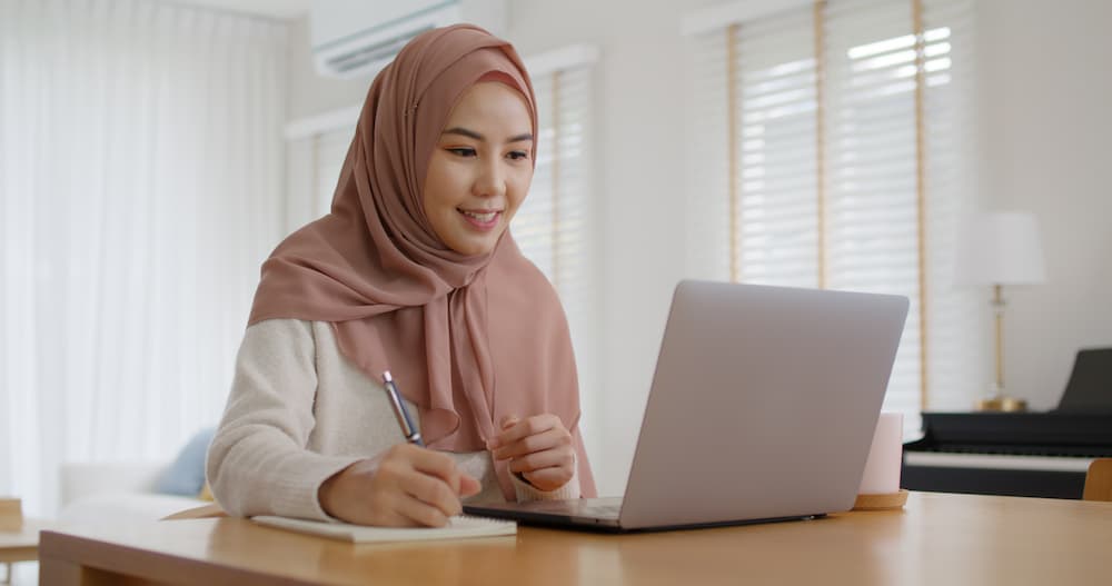 A woman making notes in front of a laptop